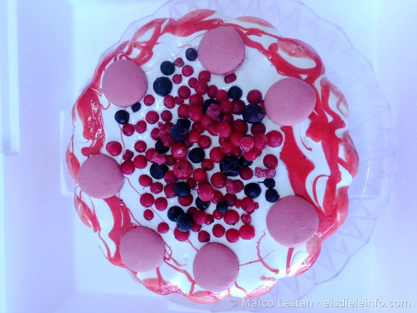 Weiße Eistorten-Dekoration mit rotem Fruchtcoulis, rosa Macarons und frischen Waldbeeren