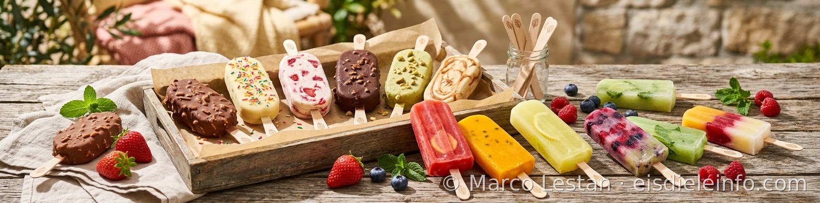 Fruchteis am Stiel und überzogenes Eis am Stiel mit Krokant, auf einem Holztisch mit frischen Früchten