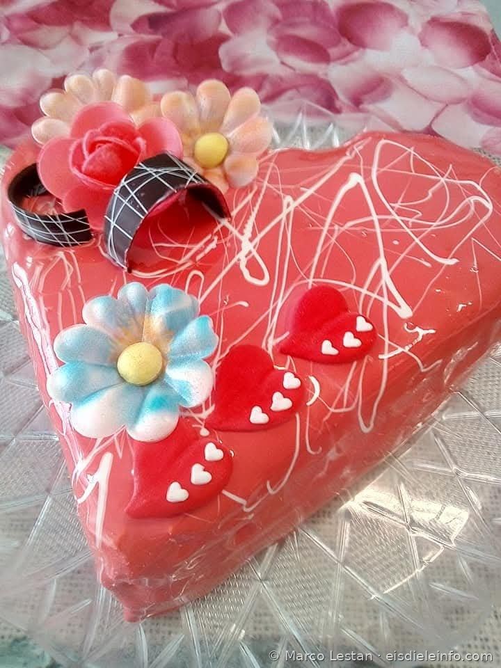 Rote herzförmige Eistorte mit Pastellblumen und dekorativen Herzchen