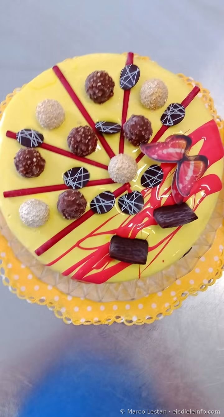 Eistorte mit gelber Glasur, Pralinen, roten Stäbchen, Schokoladenscheiben und Schmetterling
