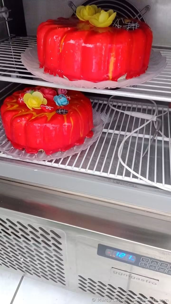 Zwei frisch glasierte Eistorten mit roter Spiegelglasur auf den Regalen eines Kühlschranks