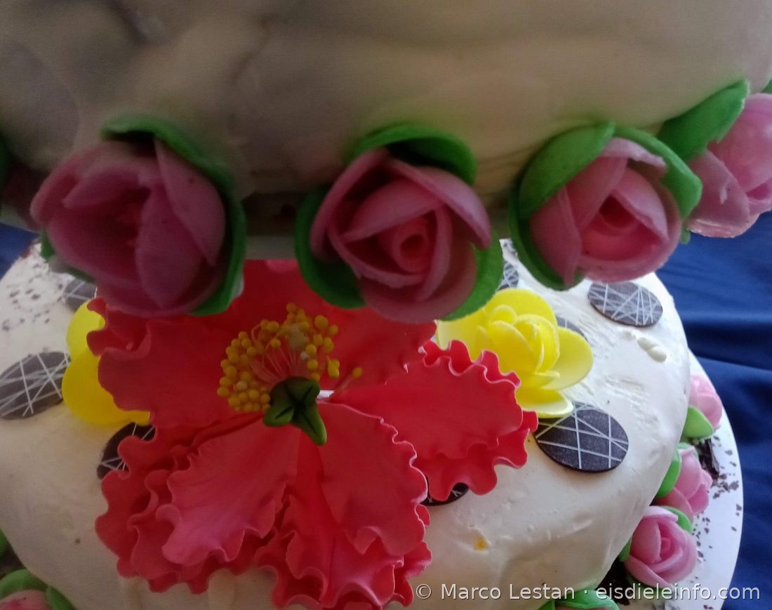 Rosa Rosenknospen mit grünen Blättern und rote Zuckerpasteblüte auf einer Hochzeits-Eistorte