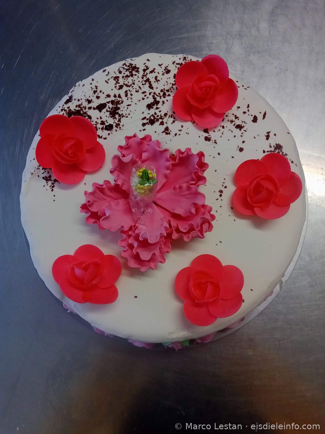Weiße Eistorte mit roten Oblatenrosen, rosa Zuckerpasteblüte und Schokoladenspänen
